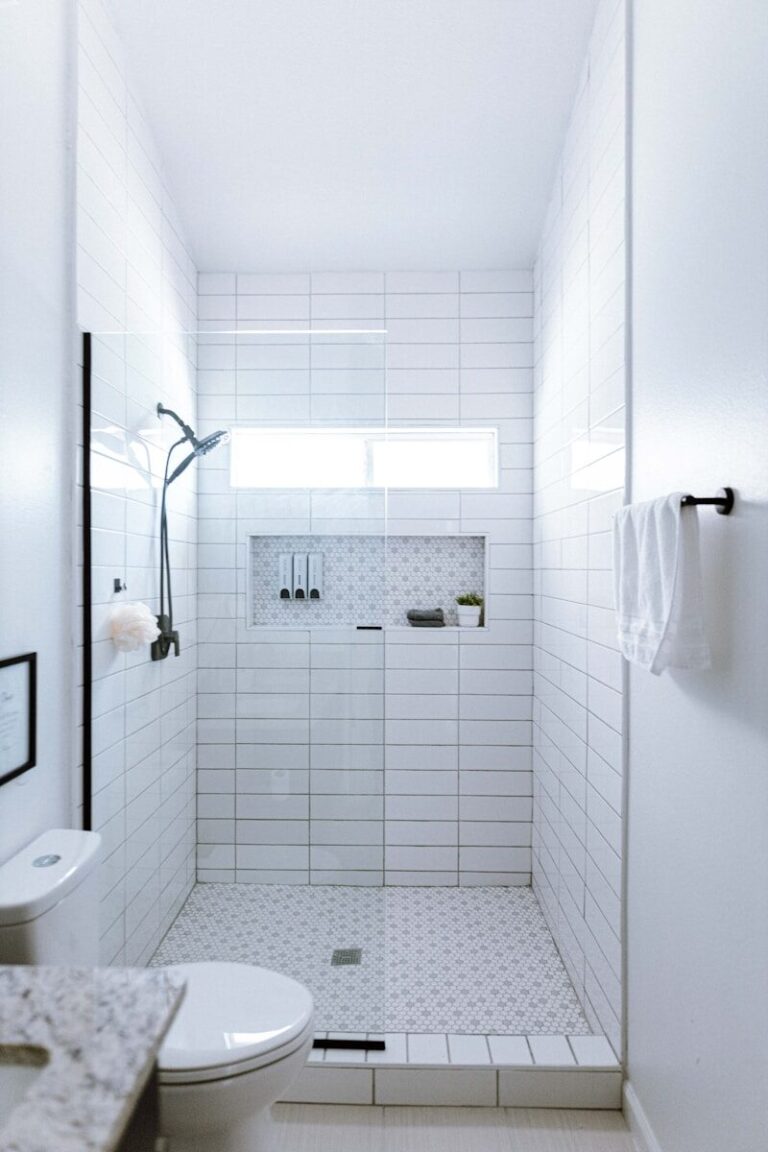 a white tiled bathroom with a shower and toilet